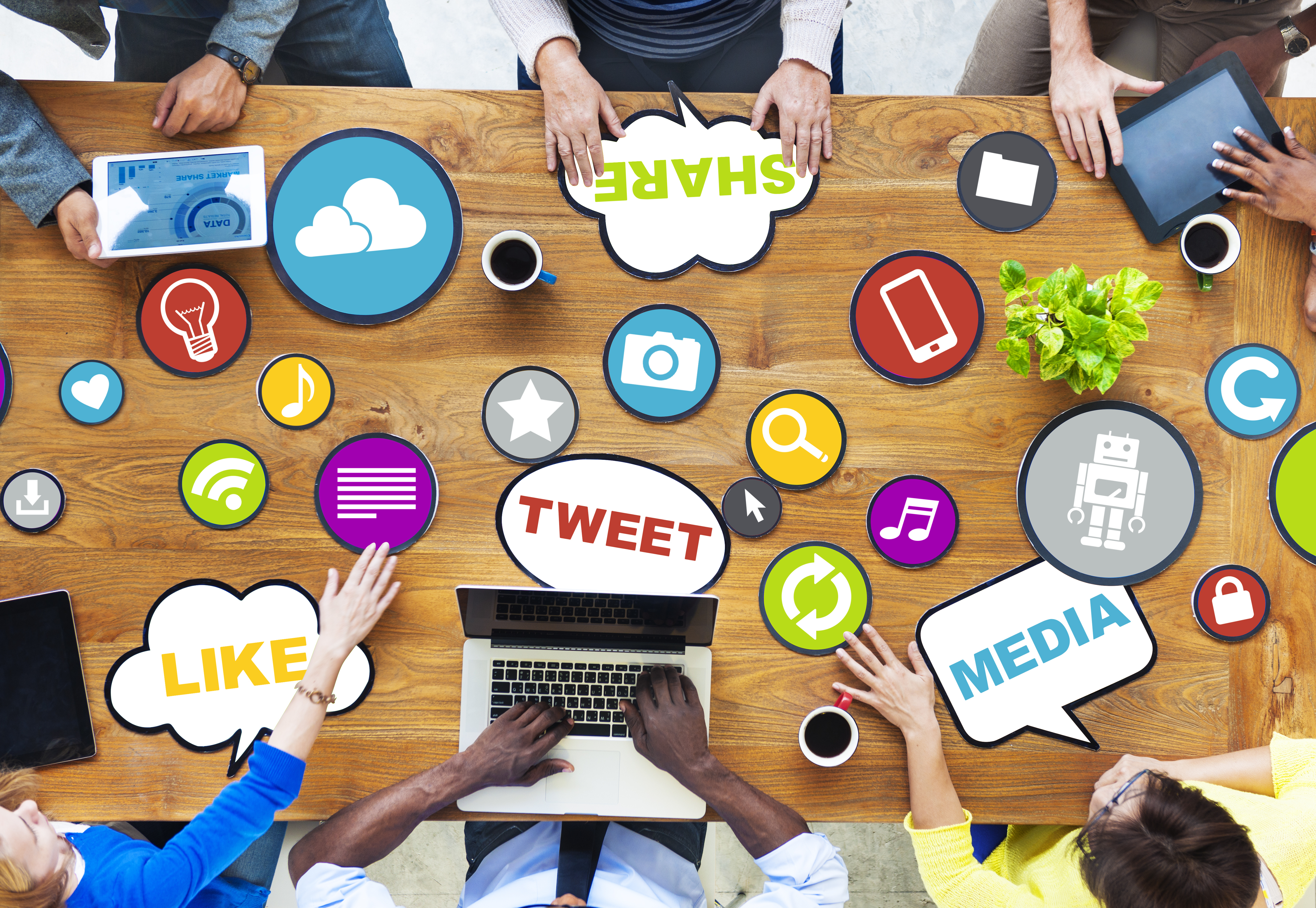 image of wooden table with social media words such as like, share, tweet, media, etc on top and a team of hands around it